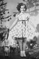 Shirley Temple, 1935 – az 1930-as évek talán legismertebb gyermek színésznője kerekített nyakú (ún. Pán Péter-nyakú) karácsonyi ruháját mutatja büszkén a kamerának.